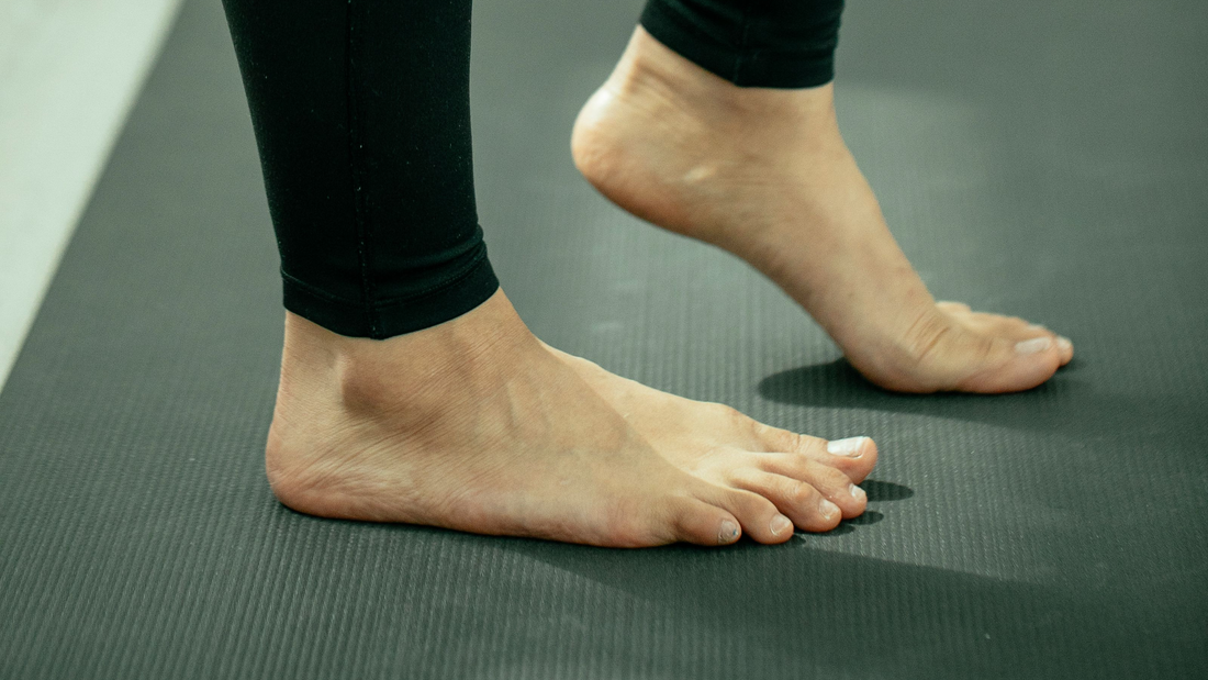 Nackte Füße einer Frau auf einer Trainingsmatte, eine Ferse angehoben