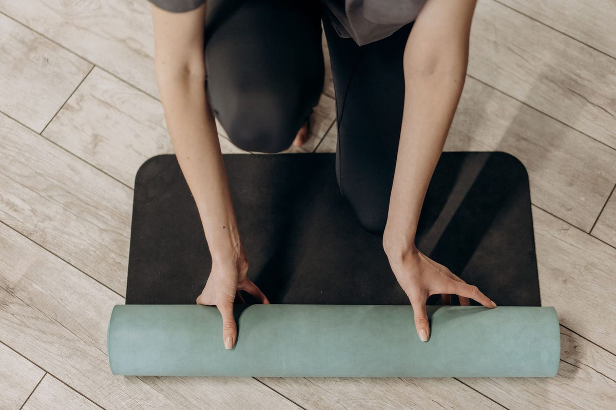 Hände rollen eine Pilates-Matte auf hellem Holzboden zusammen